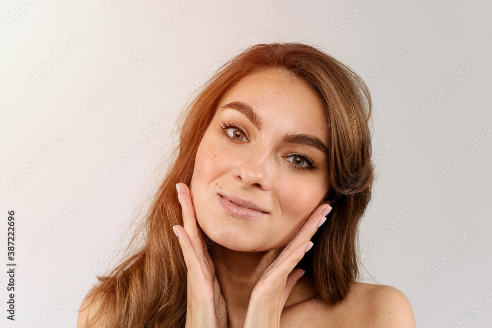 Fototapeta premium Beauty face of a young woman with hands on her cheeks. Skin care concept. Closeup portrait isolated on white background