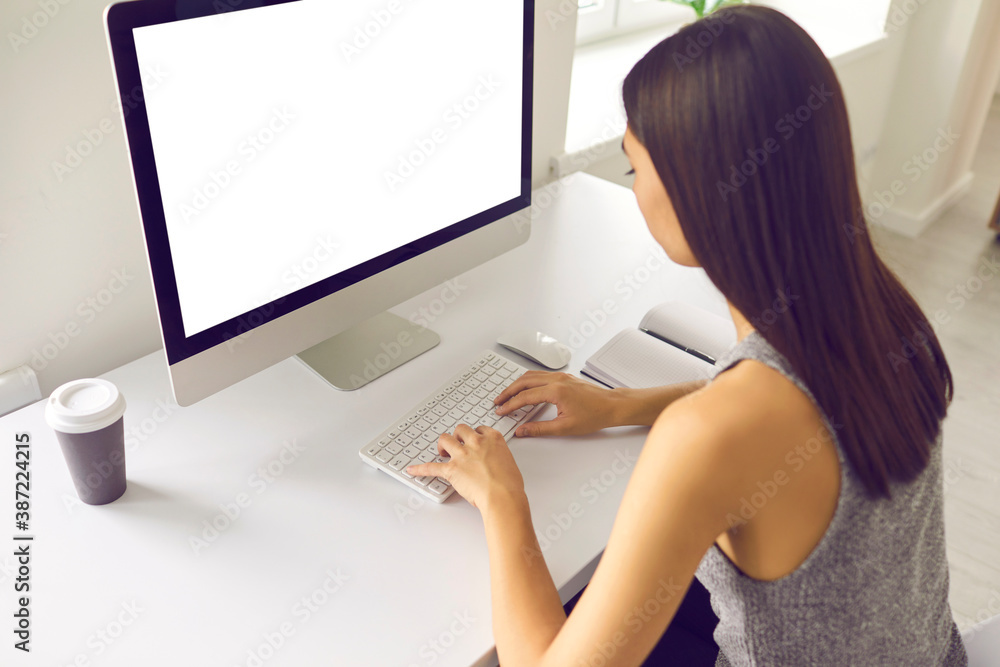Asian woman working on computer with blank white screen sitting at desk in office