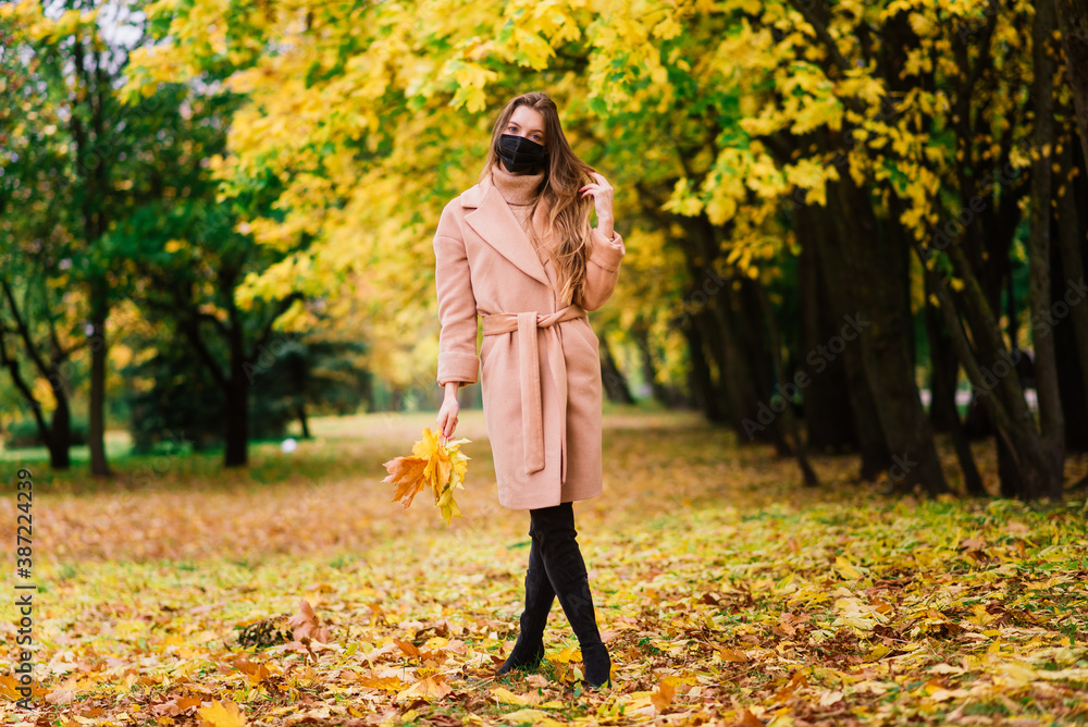 Portrait of a beautiful adult young woman on the background of autumn in park in medical face mask Portrait of a beautiful adult young woman on the background of autumn in park in medical face mask