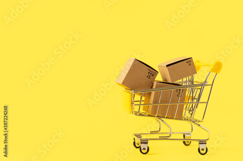Toy shopping cart with boxes in female hand over blue background. Copy space for text or design. Ssale, discount, shopaholism concept. Consumer society trend.