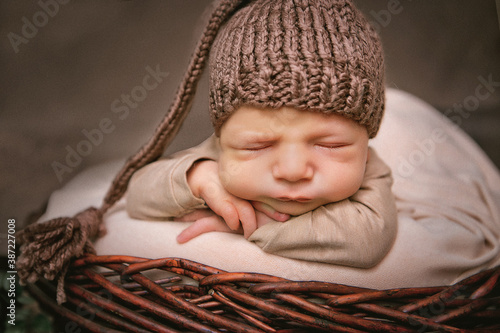 
newborn boy 12 days in a brown cap sleeps in a basket

