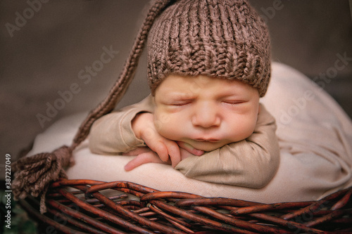 
newborn boy 12 days in a brown cap sleeps in a basket
