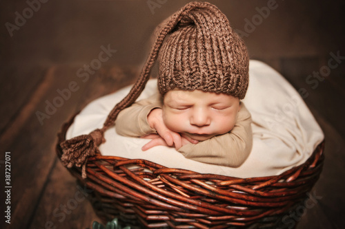 
newborn boy 12 days in a brown cap sleeps in a basket
