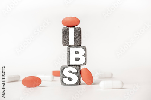 a group of white and red pills and cubes with the word IBS Irritable bowel syndrome on them, white background. Concept carehealth, treatment, therapy. photo