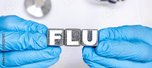 FLU - word from stone blocks with letters holding by a doctor's hands in medical protective gloves