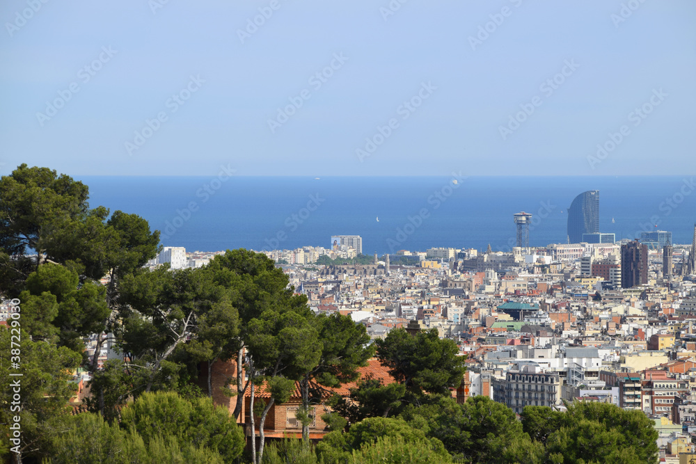In the background of the green trees is the skyline of Barcelona and the Mediterranean sea. Aerial view of the city.
