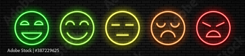 A set of five neon emoticons with different facial expressions. Joyful to angry, and in between. Green yellow orange and red colors. Against the background of a brick wall. All elements are isolated.