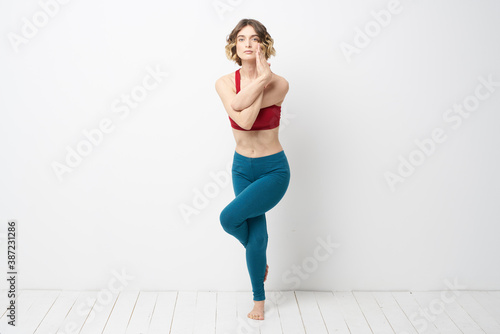 sports woman in a bright room doing yoga in full growth blue leggings and a red tank top