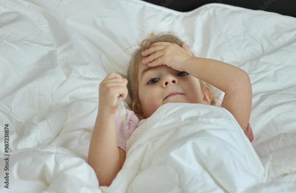 Obraz premium Sick little girl in bed with a thermometer under her arm.