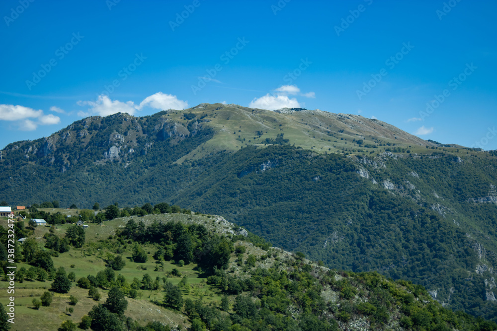 A fragment of a mountain range overgrown with green bushes and grass, a view against the background of a blue cloudy sky. Montenegro