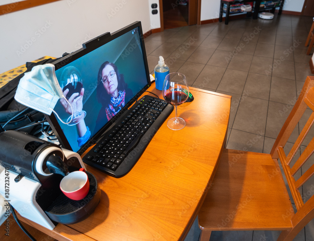 Fototapeta premium Coronavirus pandemic, social distancing means greetings and toasts are being made online. A woman is connected remotely and greets the man, they raise their wine glasses for a toast.