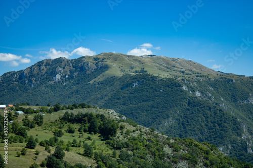 A fragment of a mountain range overgrown with green bushes and grass  a view against the background of a blue cloudy sky. Montenegro