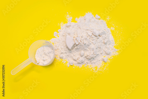 Heap of protein powder with plastic spoon on yellow background