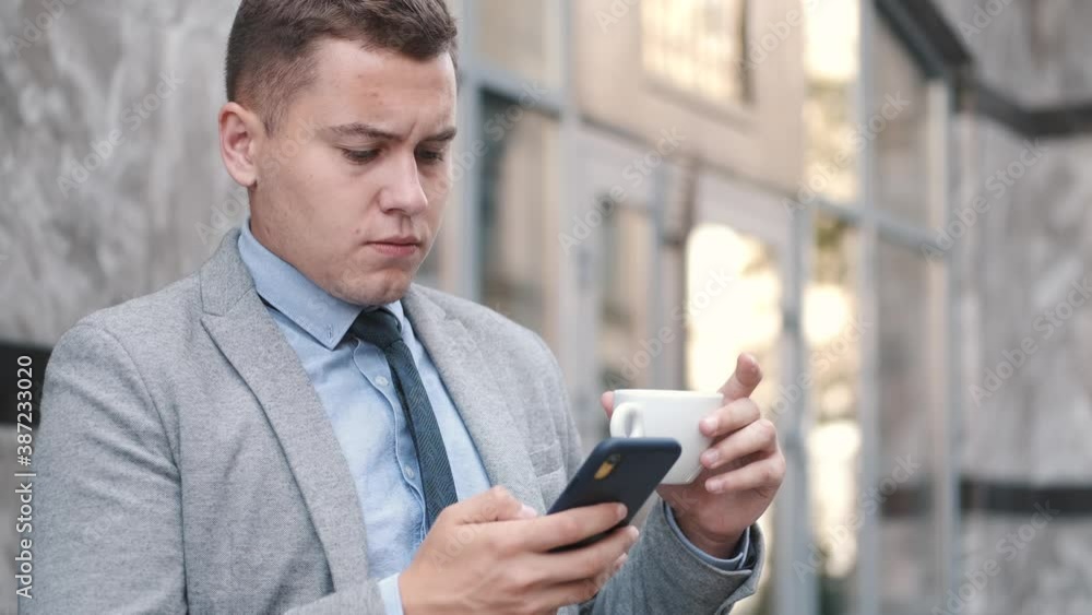 Young businessman in outsoor cafe uses the mobile phone and drinks coffee. Freelance man chatting on phone in a city. Break from work. Young businessman in outsoor cafe uses the mobile phone and drinks coffee. Freelance man chatting on phone in a city. Break from work.