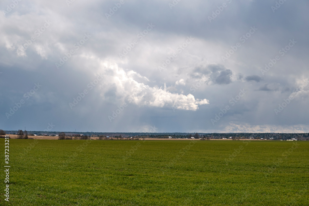 Cloudy cloudy skies on a field with green grass and rustic houses on the horizon. Cloudy cloudy skies on a field with green grass and rustic houses on the horizon.