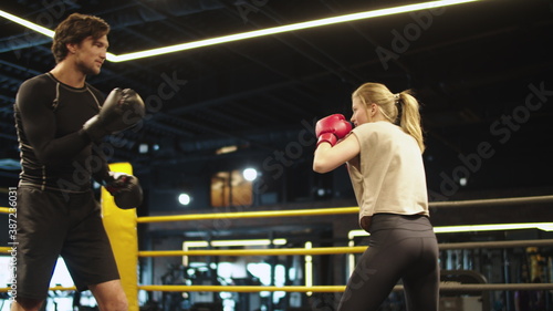 Smiling coach training with female athlete on boxing ring. Couple boxing at gym
