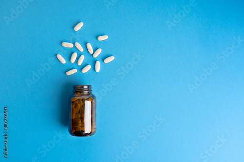 Flat lay of tablets or pills of antibiotics or aspirin aimed to prevent covid and other diseases in brown glass bottle against blue background. Image with copy space, horizontal orientation