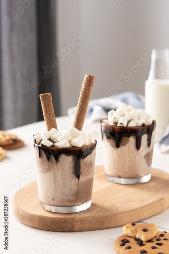 Milkshake with ice cream, marshmallows and chocolate, a glass with a milkshake on a wooden board, chocolate chip cookies and a bottle of milk