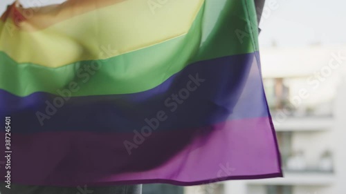 Black man holding rainbow flag and waving it behind his back from the balcony. High quality 4k footage