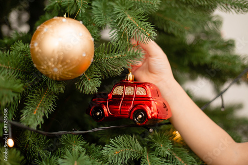 The child hangs on the Christmas tree a toy in the form of a red car, a close-up. Christmas concept, text space