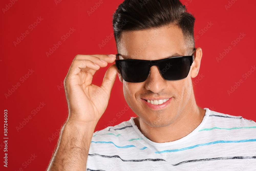 Handsome man wearing sunglasses on red background, closeup