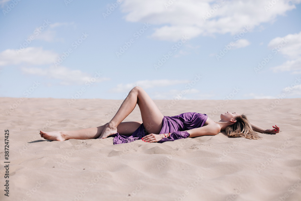 Young, slender girl with purple cloth poses in the desert