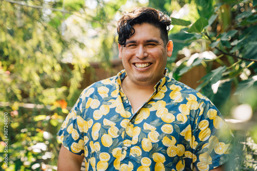 Portrait of happy, smiling latinx man in bright patterned shirt standing outside in garden photo