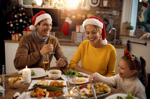 Cheerful parents and their daughter enjoying in Christmas lunch at dining table.