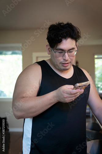 Young latinx man in workout tank top checking text messages on phone