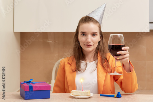 A young woman says a toast with a glass of wine in her hand. On the table is a birthday cake with a burning candle.