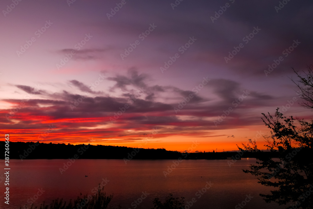 Amazing sunset over the water. Beautiful landscape with a lake and dramatic sky with cumulus clouds on the horizon.
