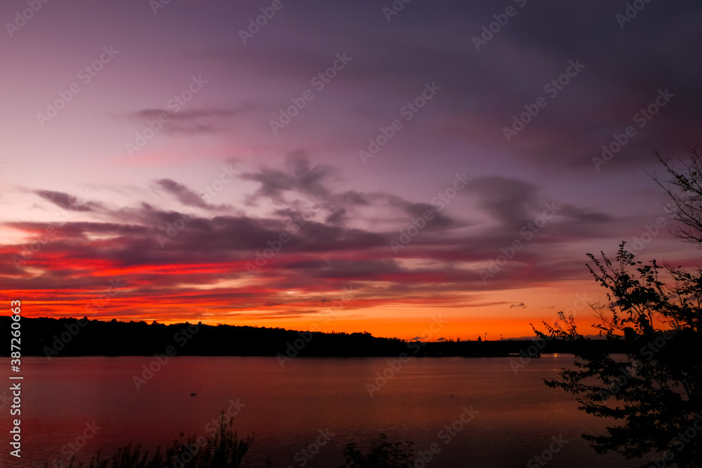 Fototapeta premium Amazing sunset over the water. Beautiful landscape with a lake and dramatic sky with cumulus clouds on the horizon.