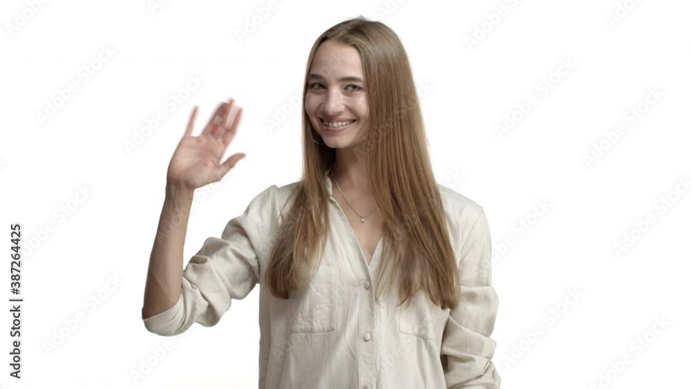 Video of friendly adult woman with braces and necklace, wearing beige blouse, saying hello and waving hand to greet you, smiling happy, standing over white background Video of friendly adult woman with braces and necklace, wearing beige blouse, saying hello and waving hand to greet you, smiling happy, standing over white background