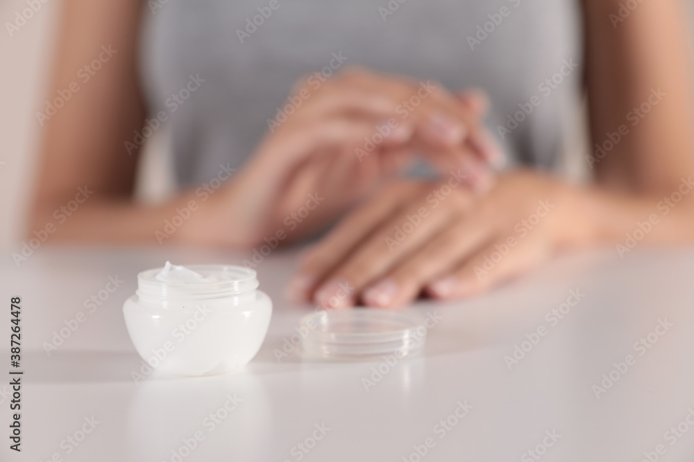 Young woman at table, focus on jar with cream Young woman at table, focus on jar with cream