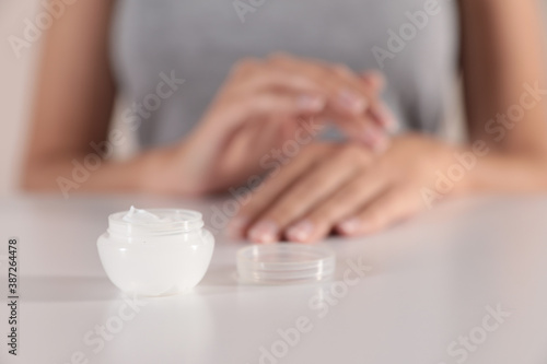 Young woman at table, focus on jar with cream