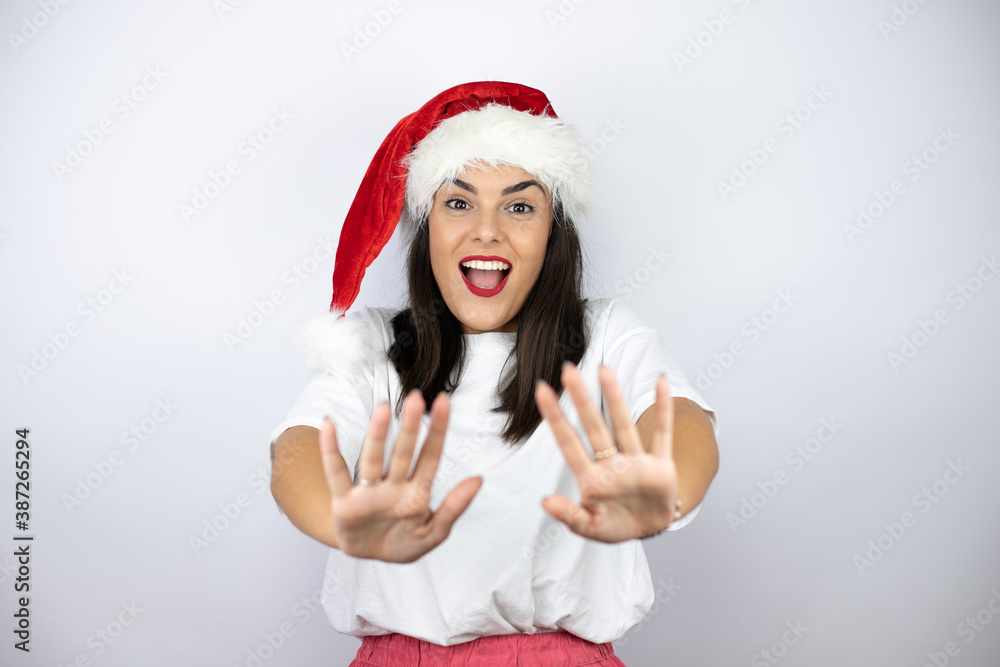 Young beautiful woman wearing a christmas hat over white background afraid and terrified with fear expression stop gesture with hands, shouting in shock. Panic concept. Young beautiful woman wearing a christmas hat over white background afraid and terrified with fear expression stop gesture with hands, shouting in shock. Panic concept.
