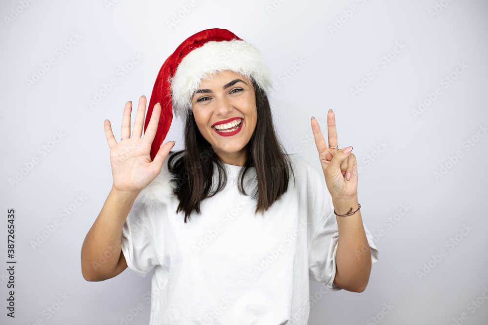 Young beautiful woman wearing a christmas hat over white background showing and pointing up with fingers number seven while smiling confident and happy Young beautiful woman wearing a christmas hat over white background showing and pointing up with fingers number seven while smiling confident and happy