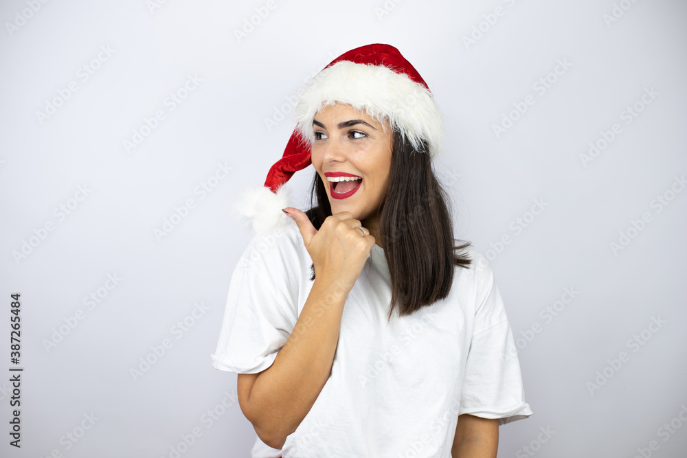 Young beautiful woman wearing a christmas hat over white background pointing with hand and finger to the side Young beautiful woman wearing a christmas hat over white background pointing with hand and finger to the side