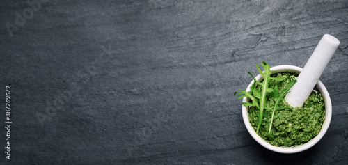 Top view of mortar with tasty arugula pesto on black table, space for text. Banner design