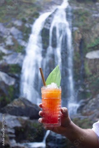 Bartender holding cocktail of orange and red colors with waterfall in the background