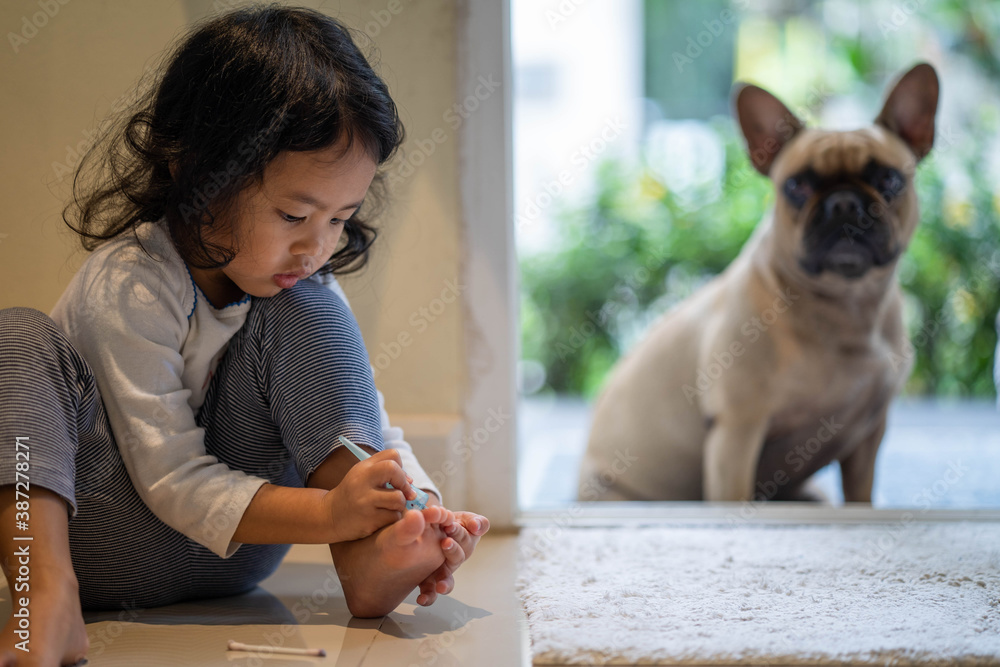 Cute little girl painting her toe-nails with her dog indoor.