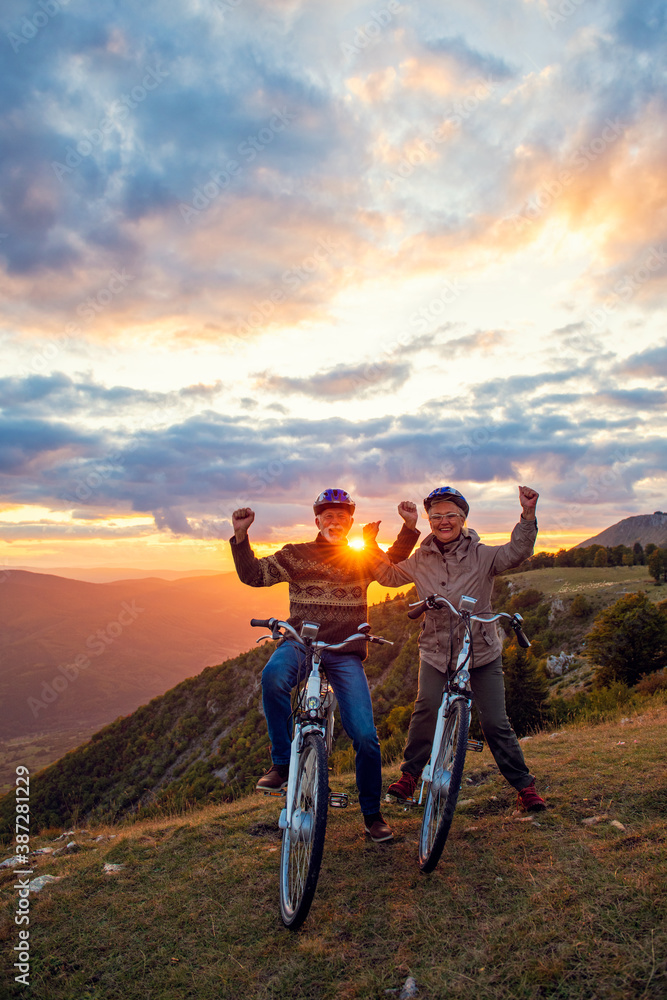 Fototapeta premium Happy senior couple riding bicycles at park and raising hands