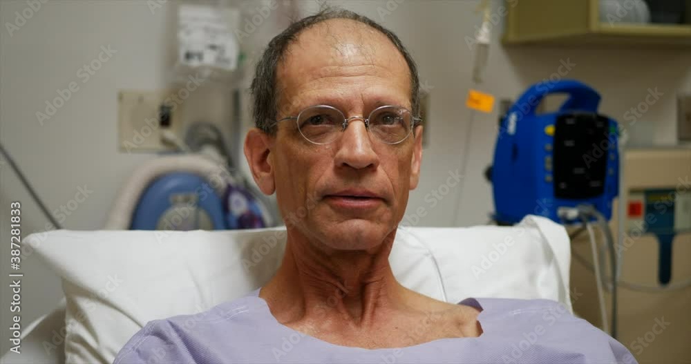 An older middle aged man in a hospital bed preparing for a minor surgery operation to test for cancer while remaining happy, positive and full of hope and optimism. An older middle aged man in a hospital bed preparing for a minor surgery operation to test for cancer while remaining happy, positive and full of hope and optimism.