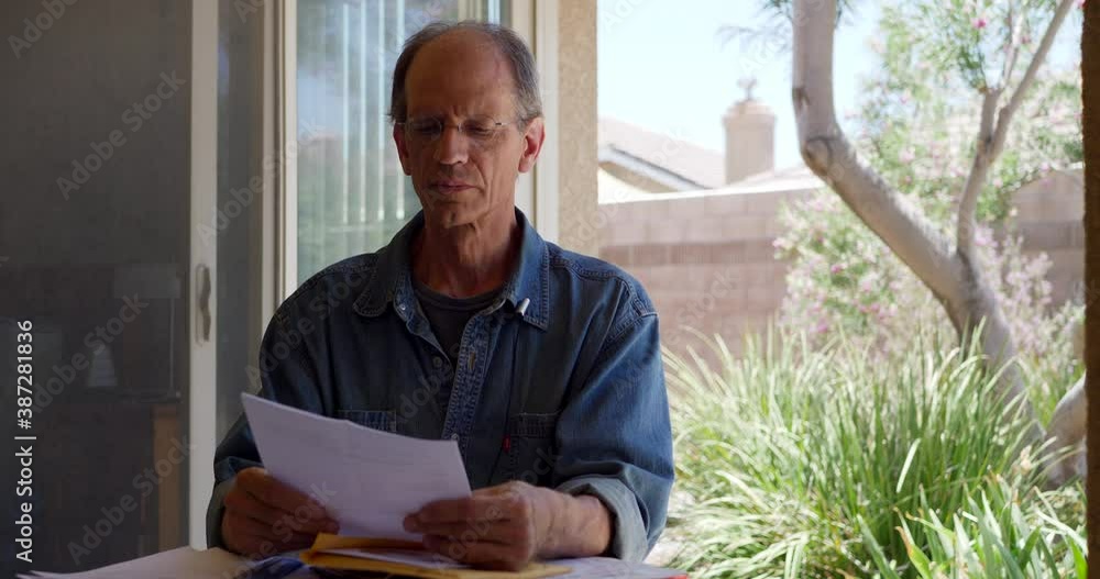 An older middle aged man reading a medical letter giving him bad news that he has been diagnosed with cancer and looking calm and sad but remaining hopeful, positive and optimistic.