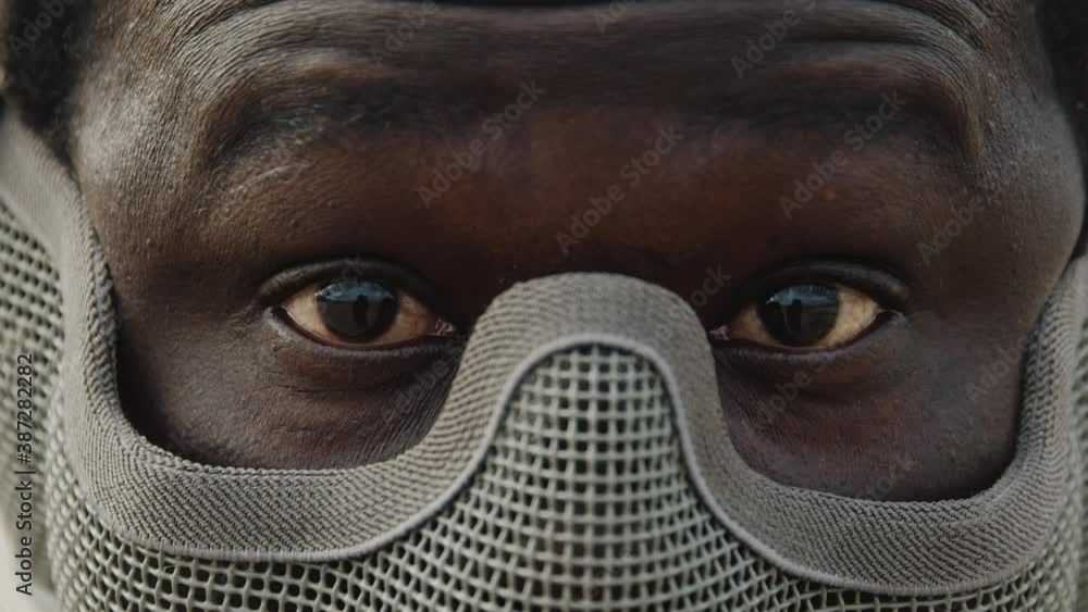 African Man Looking At Camera Wearing A Grey Metal Mesh Half Face Airsoft Mask. - close up shot African Man Looking At Camera Wearing A Grey Metal Mesh Half Face Airsoft Mask. - close up shot