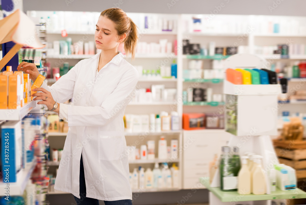 Young pharmacist is browsing rows of body care products in pharmacy