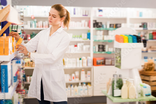 Young pharmacist is browsing rows of body care products in pharmacy