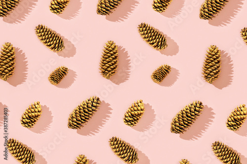 Christmas pattern from natural pine cone painted golden colored on pink.