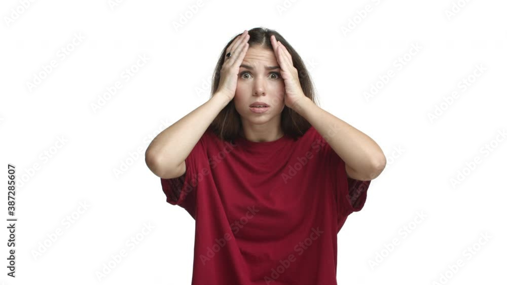 Shocked girl in red t-shirt looking ambushed, holding hands on head and gasping alarmed, standing over white background Shocked girl in red t-shirt looking ambushed, holding hands on head and gasping alarmed, standing over white background