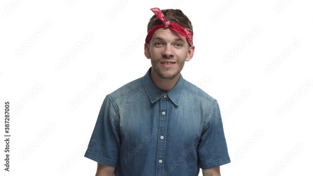 Handsome young hipster guy with red bandana and beard, looking closer at something and starting to laugh, smiling happy, standing pleased over white background Handsome young hipster guy with red bandana and beard, looking closer at something and starting to laugh, smiling happy, standing pleased over white background